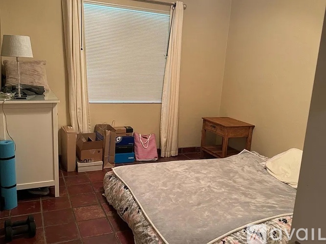 A bedroom with a bed, nightstand, and window with blinds.