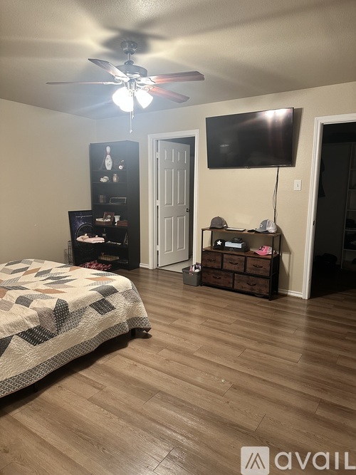 A bedroom with a bed, a ceiling fan, and a TV mounted on the wall.