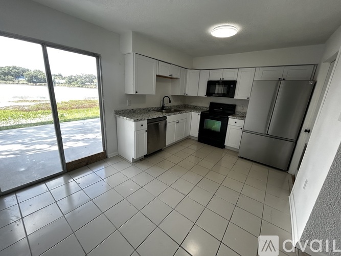 A kitchen with white cabinets and appliances, a large window, and a tiled floor.