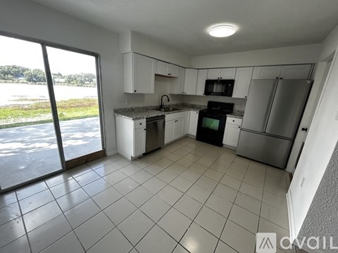 A kitchen with white cabinets and appliances, a large window, and a tiled floor.