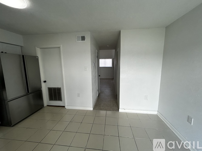 A kitchen area with a refrigerator, a door, and a hallway.