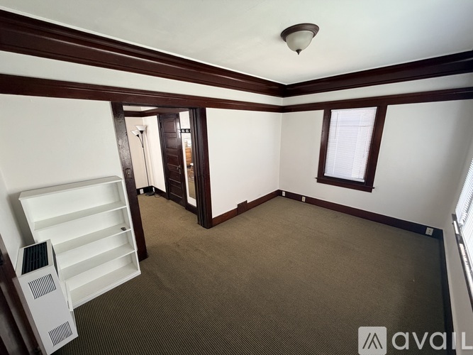 A room with a carpeted floor, a window with blinds, and a white cabinet with drawers.