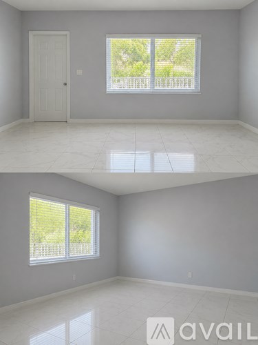 A room with a white door and a window with a view of a fence and trees.
