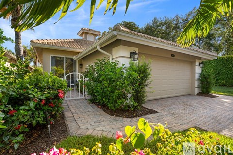 A house with a driveway and a gate surrounded by greenery and flowers.