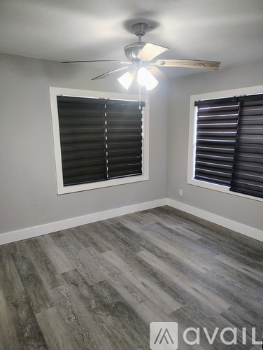 A room with a ceiling fan and two windows with blinds.