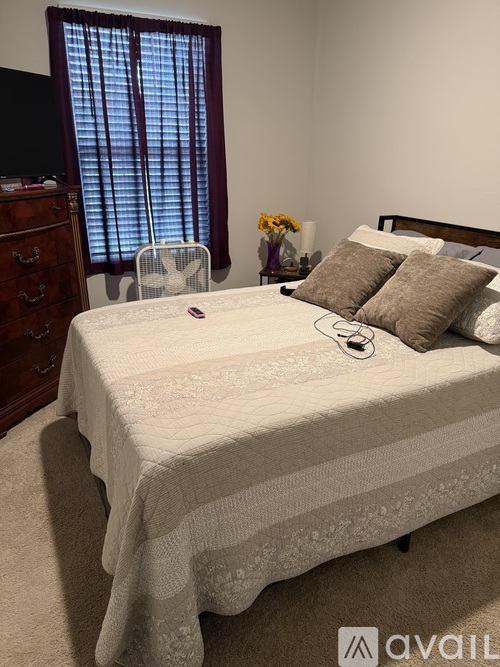 A bedroom with a bed, a dresser, and a window with blinds.