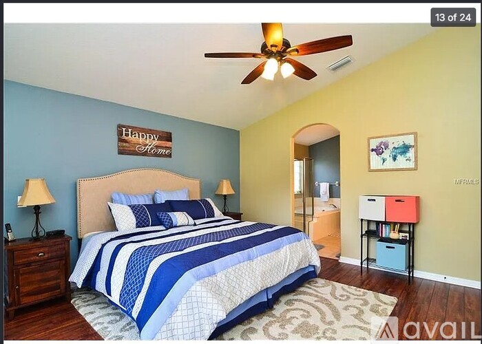 A bedroom with a bed, a ceiling fan, and a nightstand with a lamp.