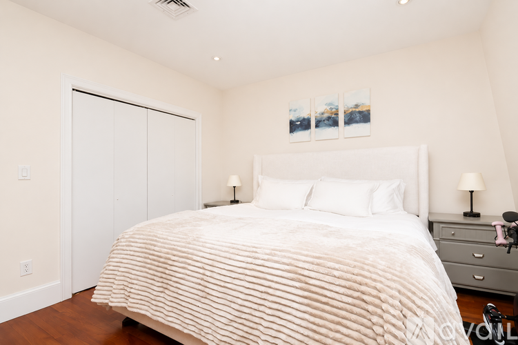A bedroom with a large bed, a nightstand with a lamp, and a painting on the wall.