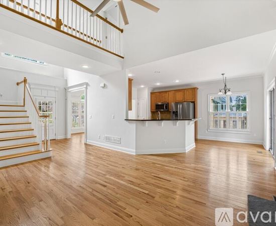 A spacious living room with wooden floors and a staircase leading to the upper level.