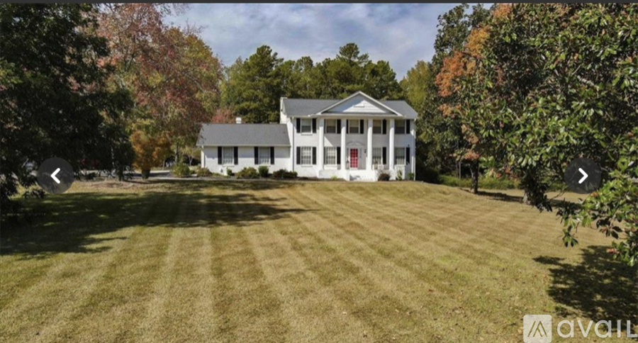 A large white house with a red door is surrounded by a grassy lawn and trees.