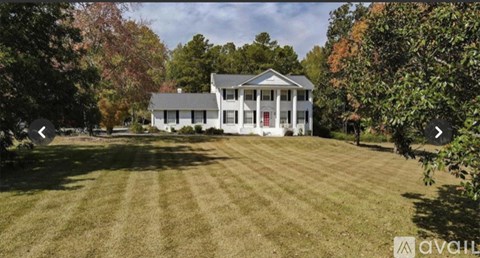 A large white house with a red door is surrounded by a grassy lawn and trees.