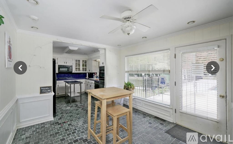 A room with a table and chairs in the foreground and a kitchen in the background.