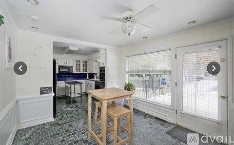 A room with a table and chairs in the foreground and a kitchen in the background.