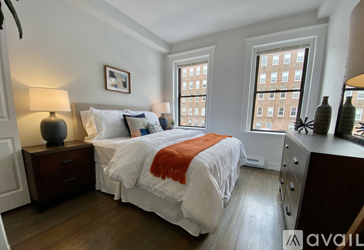 A bedroom with two beds, one with an orange throw, and a window showing a city view.