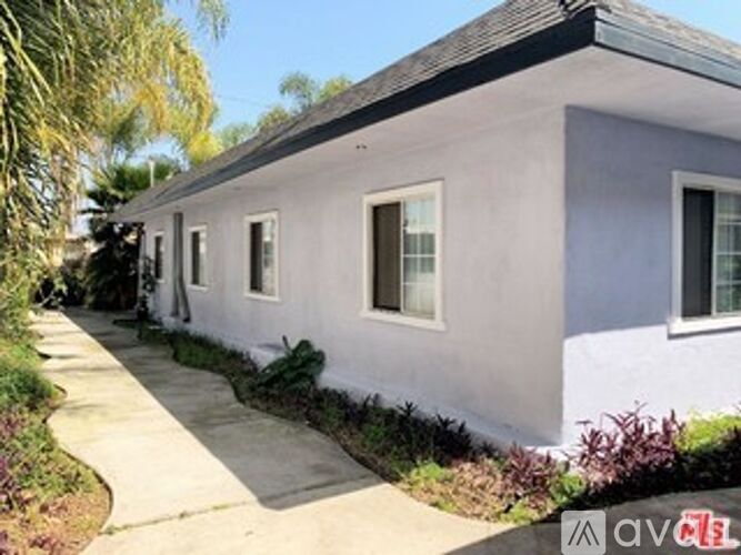 A small white house with a grey roof and a grey concrete walkway.