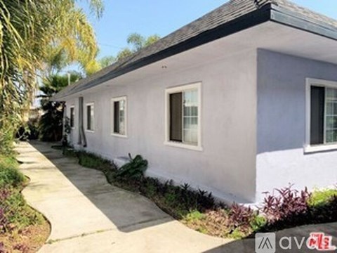 A small white house with a grey roof and a grey concrete walkway.