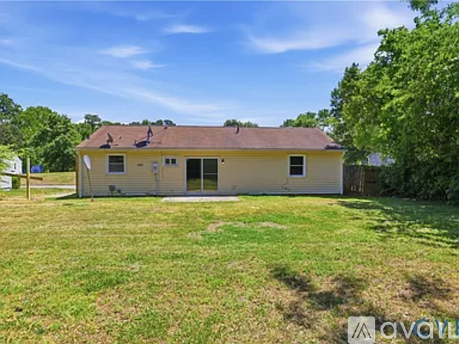 A house with a brown roof and a white wall is surrounded by a grassy area.