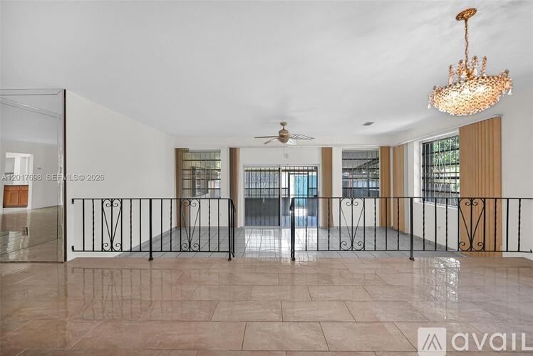 A spacious room with a chandelier, a ceiling fan, and a black metal railing.