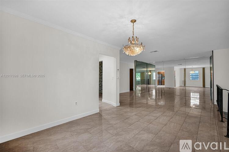 A spacious, empty room with a chandelier and tiled flooring.