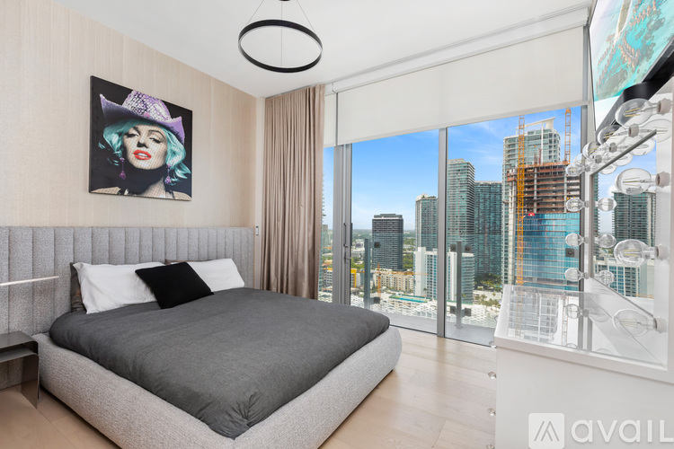 A bedroom with a large bed and a city view through the window.