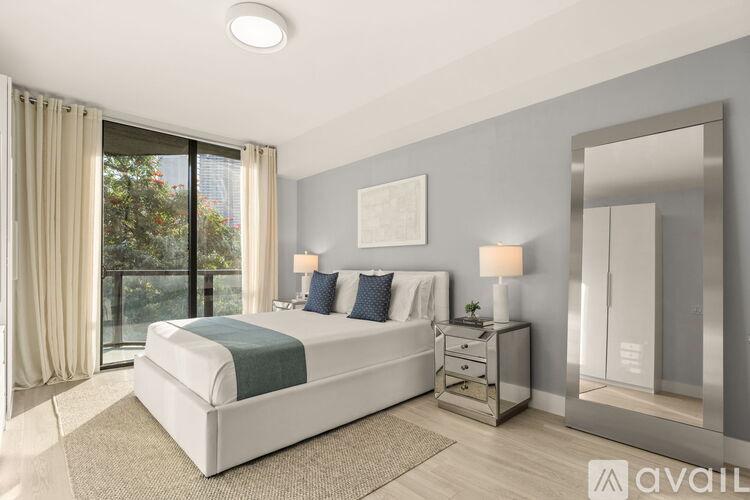 A bedroom with a large bed, a nightstand with a lamp, and a mirror on the wall.