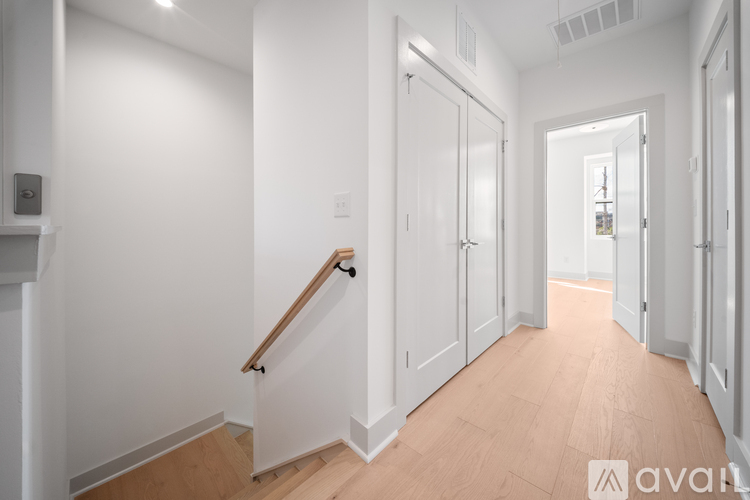 A hallway with white walls and wooden floors leading to a door.