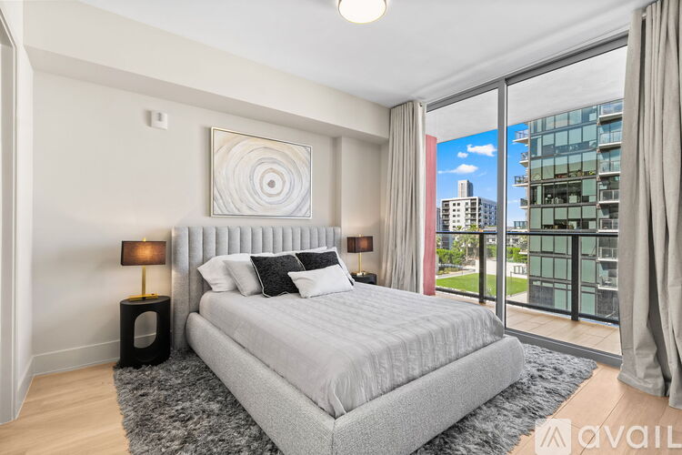 A bedroom with a large bed, a nightstand with a lamp, and a view of the city outside the window.
