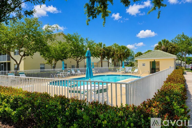 A pool surrounded by a white fence and green bushes.