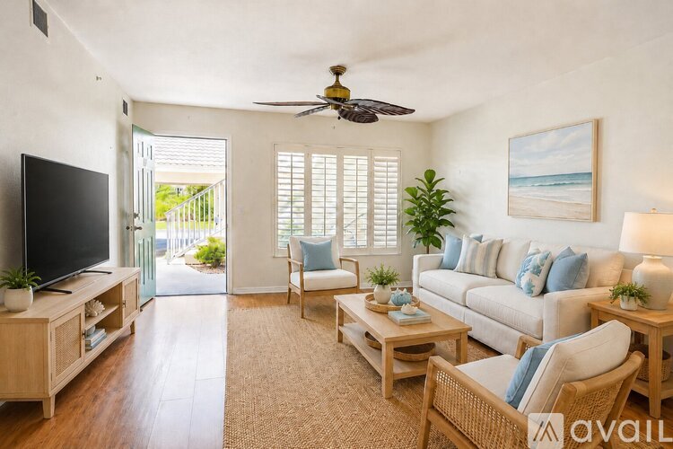 A living room with a television, a couch, a chair, a table, and a ceiling fan.
