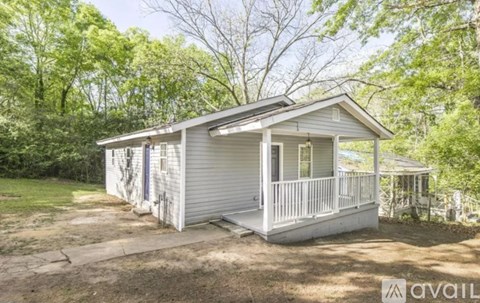 A small house with a porch is surrounded by trees.