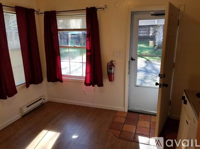 A room with a door, a window with red curtains, and a fire extinguisher on the wall.