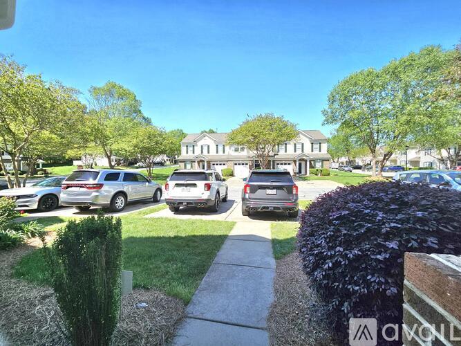 A sunny day in a residential area with cars parked on the street and houses in the background.