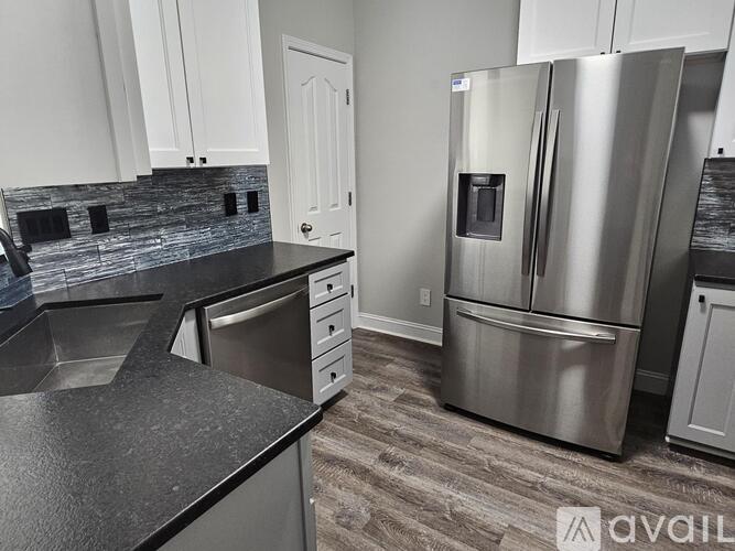 A modern kitchen with a stainless steel refrigerator and black countertops.