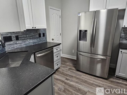 A modern kitchen with a stainless steel refrigerator and black countertops.