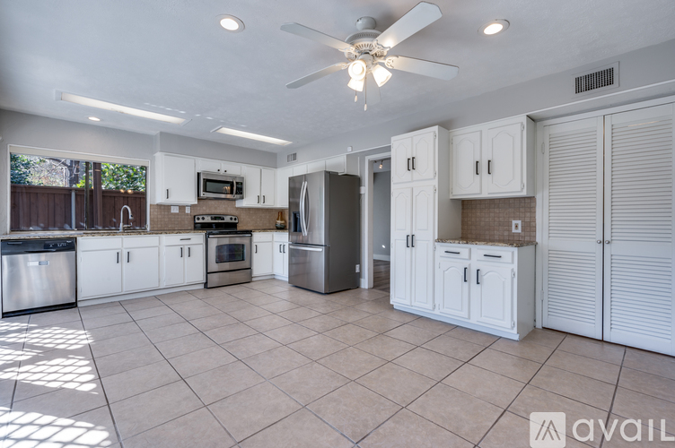 A kitchen with white cabinets and appliances, a ceiling fan, and a tiled floor.
