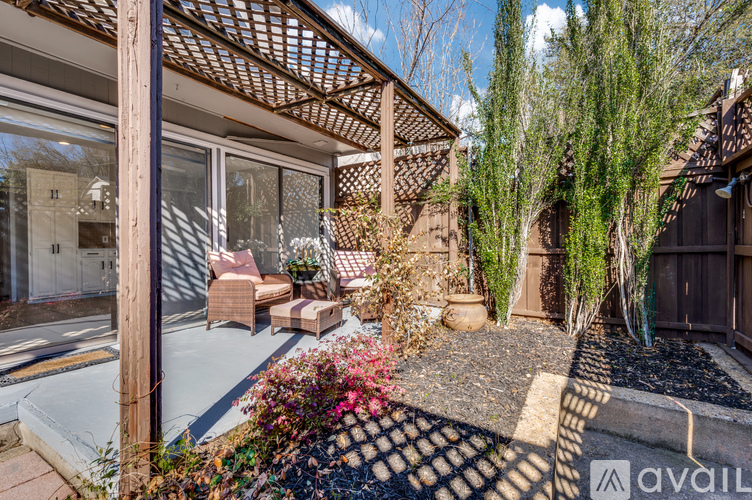 A patio with a table and chairs is surrounded by plants and trees.