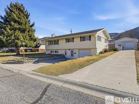 A two-story house with a garage is situated in a residential area with a tree and a mountain in the background.