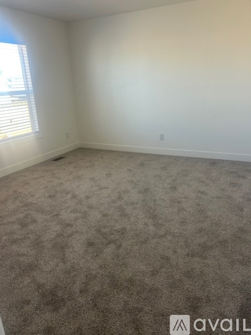A carpeted room with a window and a wall outlet.