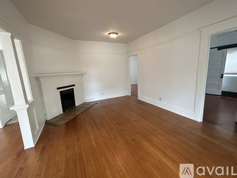 A spacious room with wooden floors and a fireplace.