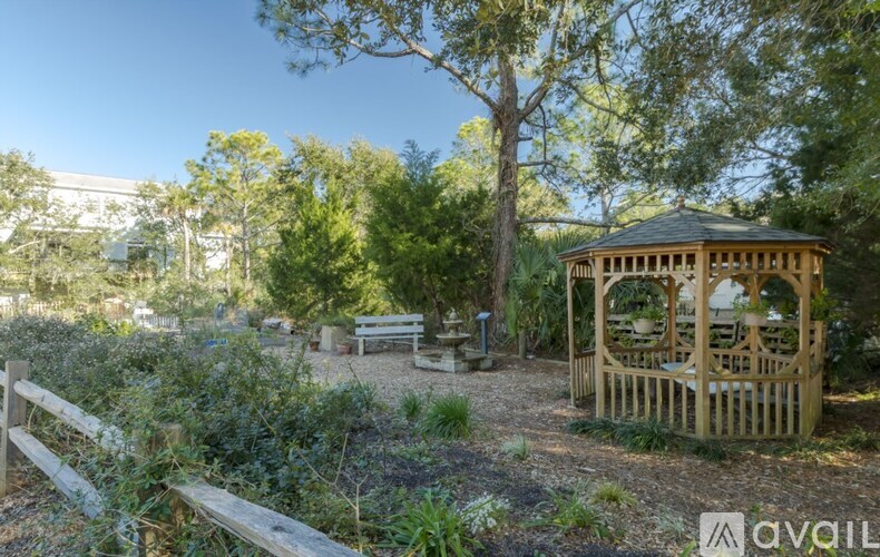 A wooden gazebo sits in a garden with a bench and a fence.