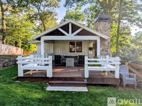 A white gazebo with a stone chimney is surrounded by a wooden deck and white chairs.