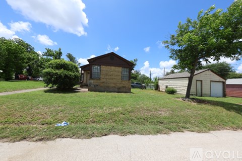A house with a brown roof and a white door is surrounded by a grassy area and trees.