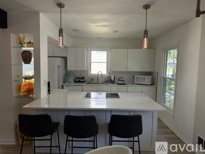 A kitchen with white cabinets and a large island with three chairs.