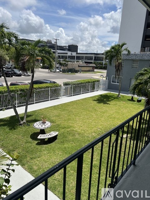 A balcony with a black railing overlooks a green lawn and a building.