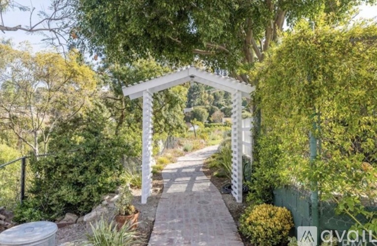 A white archway leads to a pathway surrounded by greenery.