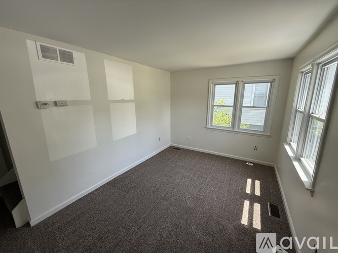A room with a carpeted floor, a window, and a wall-mounted shelf.
