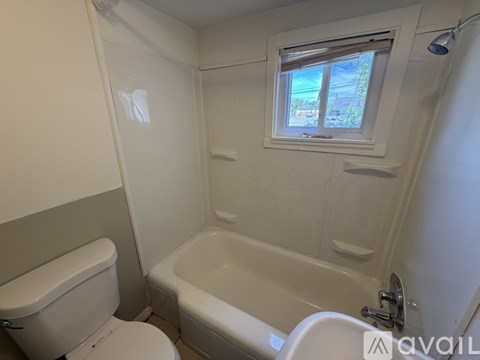A white bathroom with a toilet, tub, and window.