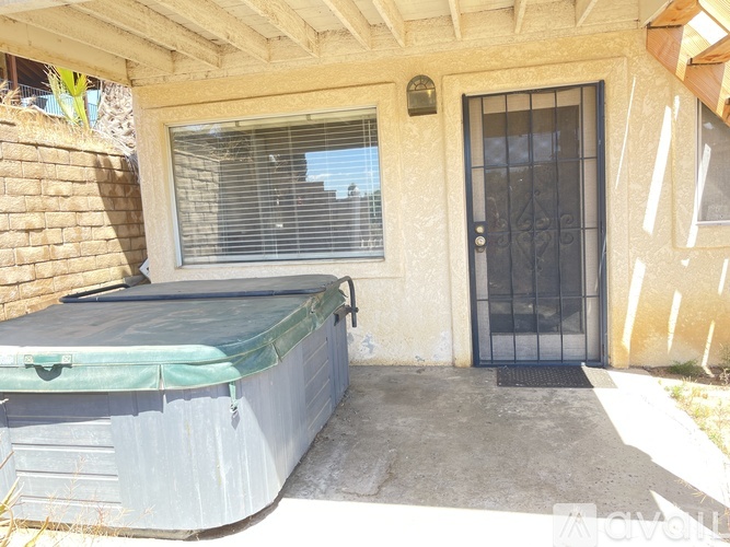 A hot tub is on the patio of a house with a black door and window.