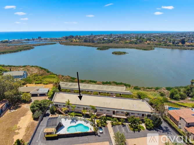 A large building with a pool in front of it is surrounded by greenery and a body of water.