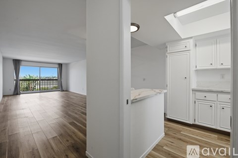 A spacious room with wooden flooring and white walls, featuring a kitchen area with white cabinets and a skylight.